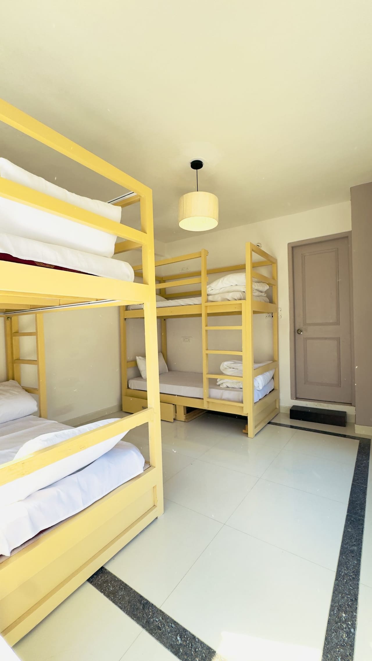 Two sets of wooden bunk beds in a bright dorm room with a pendant light