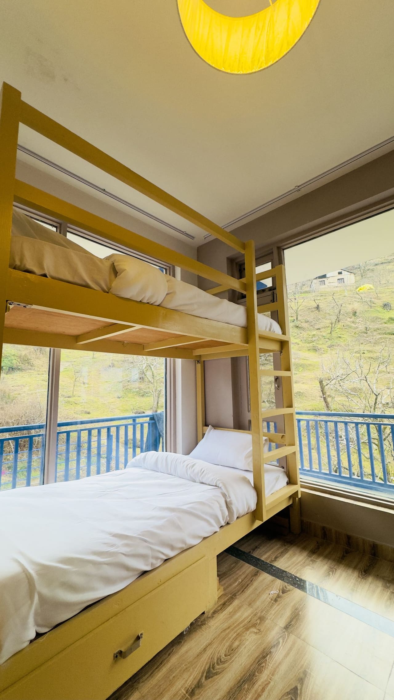 Wooden bunk beds with white linen beside a large window overlooking the orchard hillside