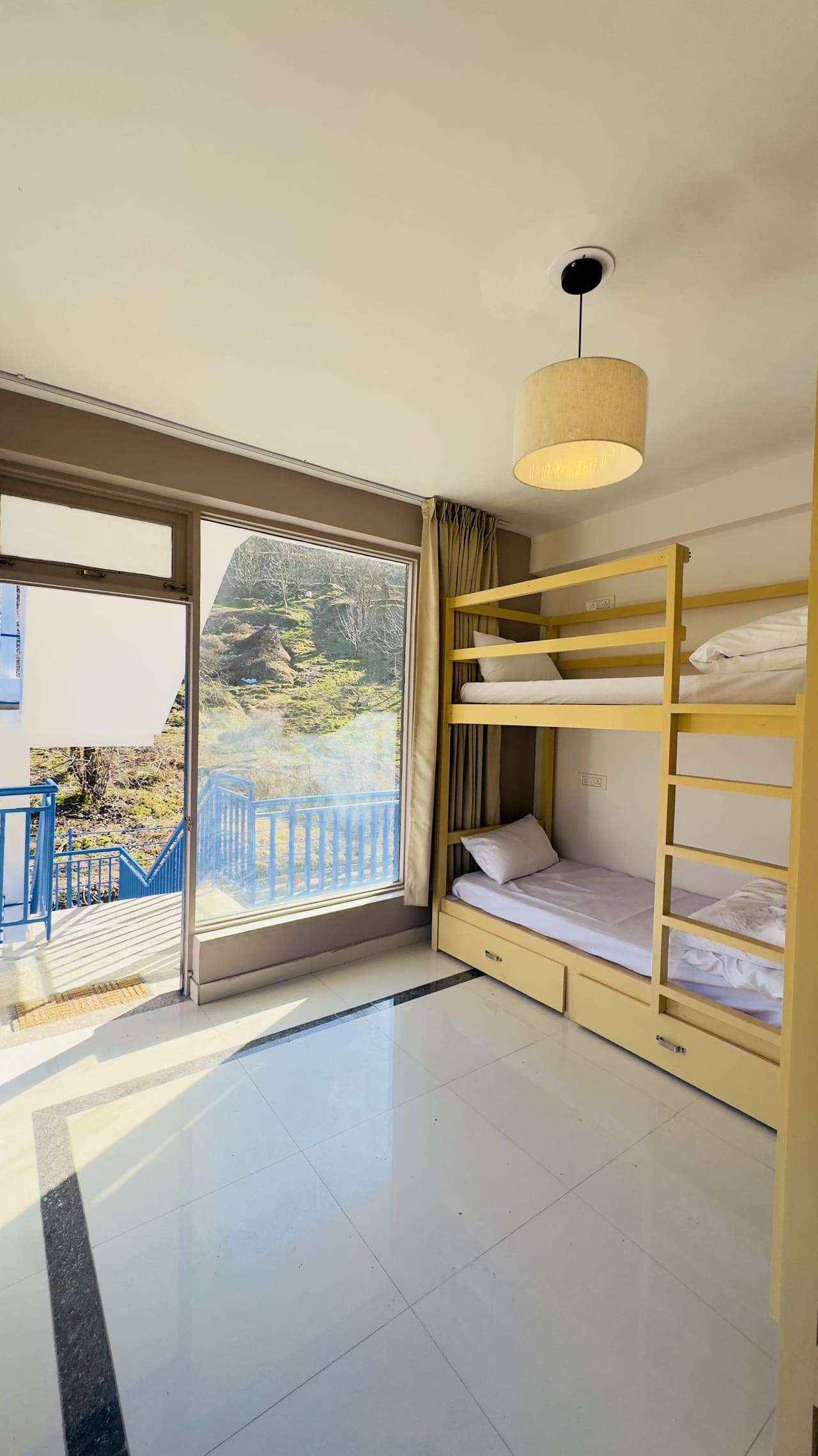 Dorm room with a bunk bed with under-bed drawers and a glass door onto a blue-railed balcony
