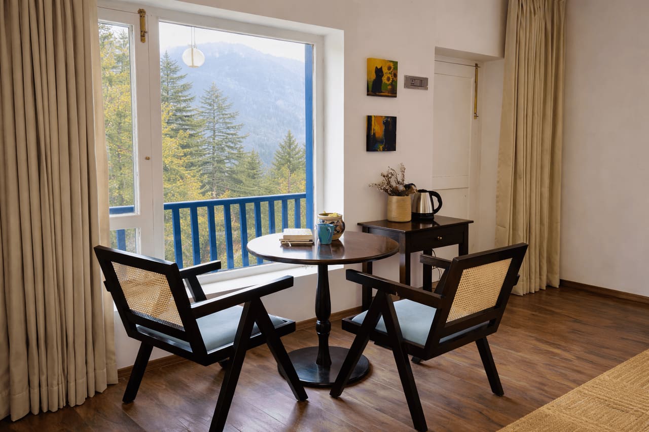 Seating area by a large window with a view of deodar-covered hills